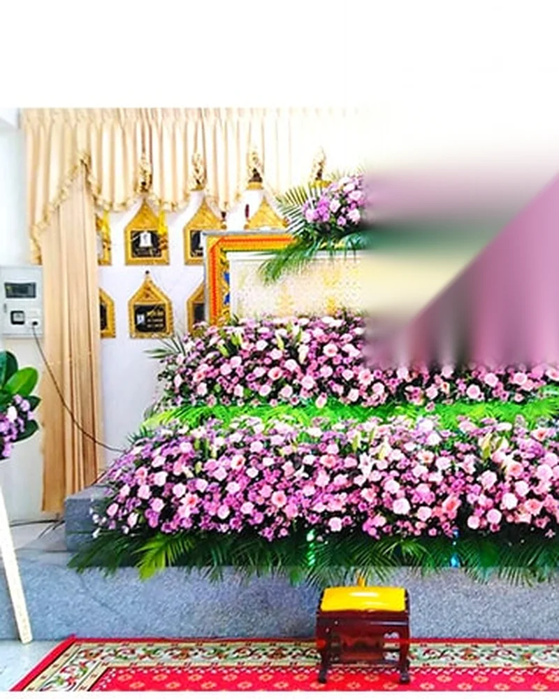 ดอกไม้สีชมพูขาวจัดประดับหน้าโลงในบรรยากาศงานพิธีม่านสีครีม