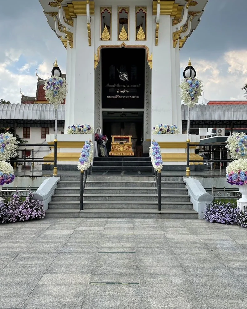 อาคารเมรุสีขาวทองประดับดอกไม้โทนม่วงขาวสองข้างบันไดทางขึ้น